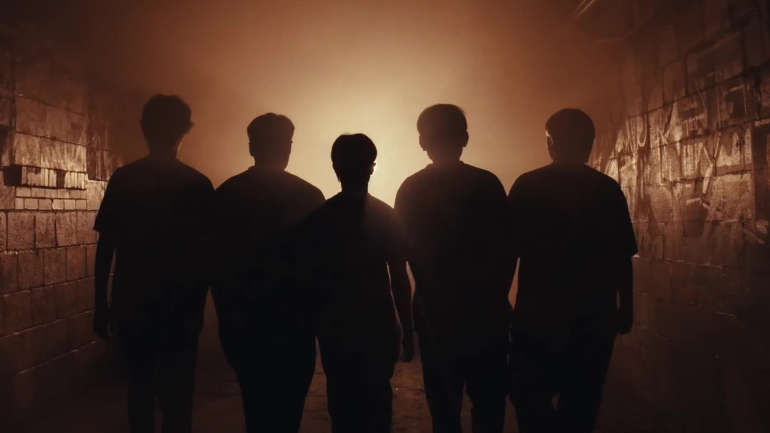 Five players walk forward into a tunnel of warm, golden light, seen only in silhouette. A powerful shot that captures unity, anonymity, and momentum.