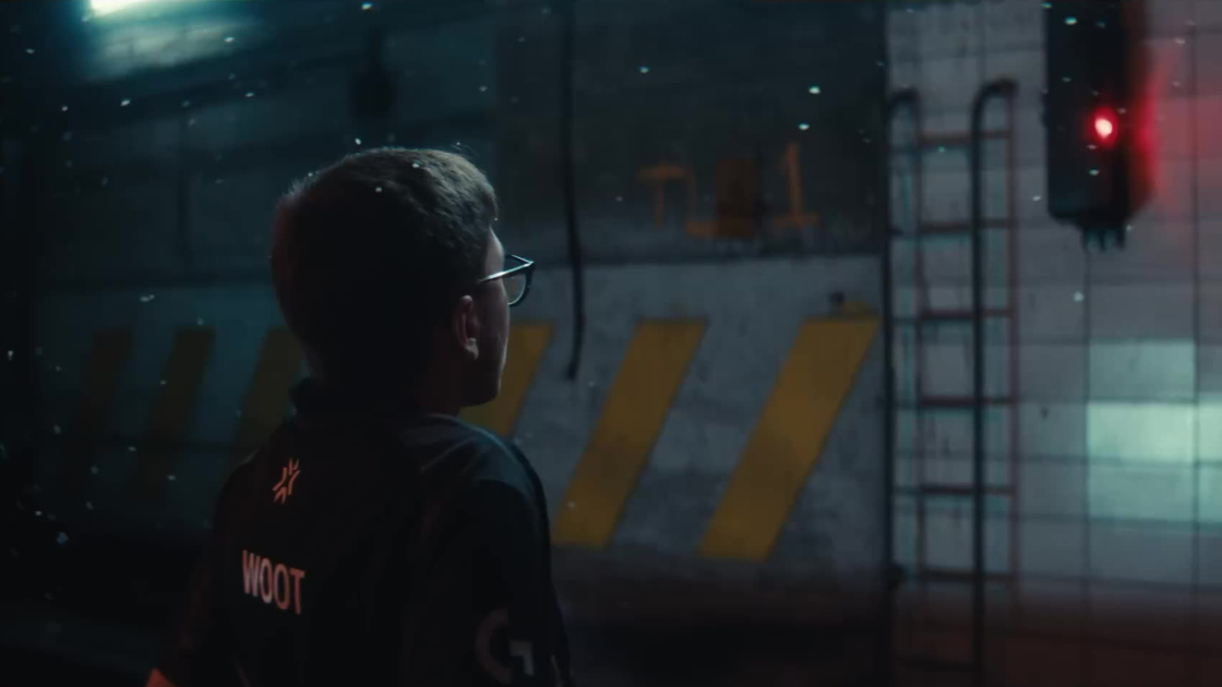 A Valorant player, jersey labeled "WOOT," gazes into a glowing red light. Snow drifts gently as he stares into the unknown — a quiet, determined moment of anticipation.