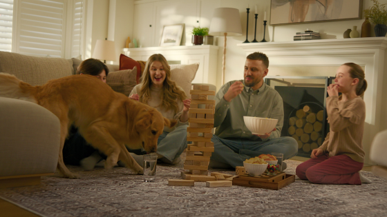 A joyful family gathers on a large living room rug to play Jenga, while the family dog joins the fun, showcasing durability without sacrificing comfort.