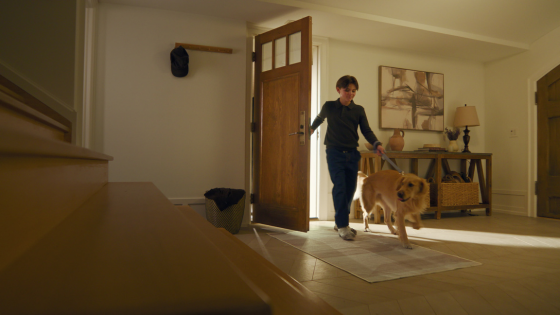 A boy walks his dog into the house, both stepping onto a Tumble rug in the entryway — a snapshot of how the brand fits seamlessly into daily routines.