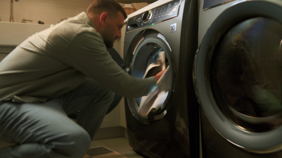 A man loads a soiled rug into the washing machine, reinforcing the brand’s core message: beautiful rugs made for real-life messes.